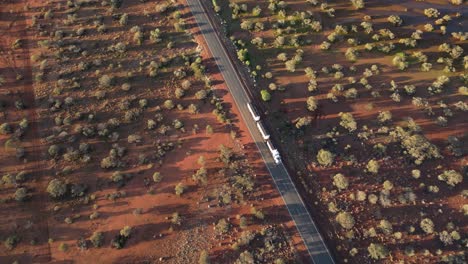 Toma-Aérea-Inclinada-Hacia-Abajo-De-Un-Camión-De-Carga-Conduciendo-Por-Una-Carretera-Rural-En-El-Desierto-Australiano-Durante-La-Puesta-De-Sol---Cámara-Lenta