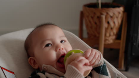 Cute-Asian-baby-in-baby-bouncer-chewing-teething-toy,-smiling-and-being-happy