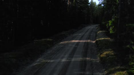 Drone-shot-following-a-dark-gravel-road-in-the-forest