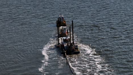 An-aerial-view-of-tugboats,-and-a-small-barge-dredging-a-bay-on-Long-Island,-New-York-on-a-sunny-day