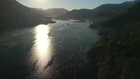 Ruhiger-See-Mit-Bewegtem-Oberflächennebel-Mit-Sonnenaufgang,-Der-Sich-Im-Wasser-Und-Bergsilhouetten-Im-Herbst-Spiegelt