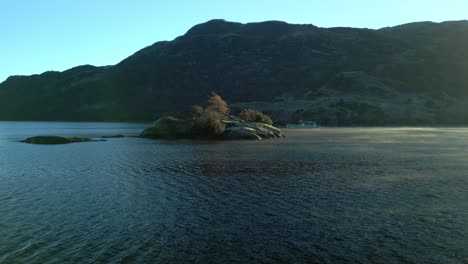 Das-Boot-Bewegt-Sich-Hinter-Einer-Kleinen-Insel-Auf-Einem-Ruhigen-See,-Während-Bei-Sonnenaufgang-Im-Herbst-Nebel-Vorbeizieht