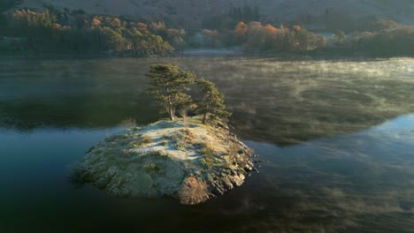 Kleine-Insel-Mit-Bäumen-In-Einem-Ruhigen-See-Mit-Bewegtem-Nebel-Bei-Sonnenaufgang-Im-Herbst