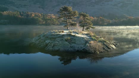 Kleine-Felsige-Insel-Mit-Zwei-Bäumen-Auf-Einem-Ruhigen-See-Und-Nebel,-Der-Sich-Bei-Sonnenaufgang-Im-Herbst-Um-Die-Insel-Windet