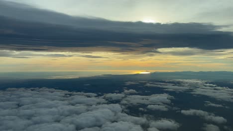 Spectacular-aerial-view-of-Valencia-city-and-coast-shot-from-an-airplane-cabin-flying-westbound-at-sunset,-with-the-sun-veiled-by-grey-clouds