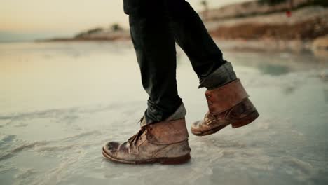 Man-with-dirty-old-leather-boots-walking-on-salty-edge-of-Dead-Sea,-Israel