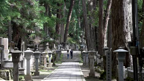 Tourist-Couple-Seen-Walking-Up-Stairs-In-Distance-Along-Path-At-Okunoin-Cemetery-In-Koya-San