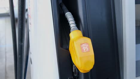 Yellow-gasoline-fuel-nozzle-rested-on-a-slot-of-a-gas-station-in-Bangkok,-Thailand