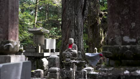 Gravestones-And-Jizo-Bosatsu-Statue-At-Okunoin-Cemetery-At-Koyasan-With-Forest-Trees-In-Background