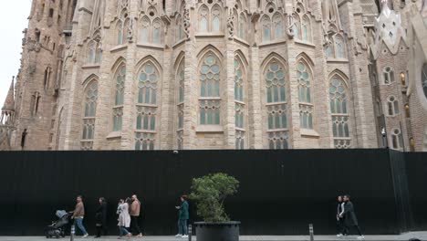 Tourists-and-pedestrians-walk-past-the-Sagrada-Familia,-the-largest-unfinished-Catholic-church-in-the-world-and-part-of-a-UNESCO-World-Heritage-Site