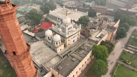 Aerial-Overhead-View-Of-Gurdwara-Dehra-Sahib-Sri-Guru-Arjan-Dev-With-Pull-Back-Shot-Past-Minaret-Tower-Of-Badshahi-mosque-In-Lahore