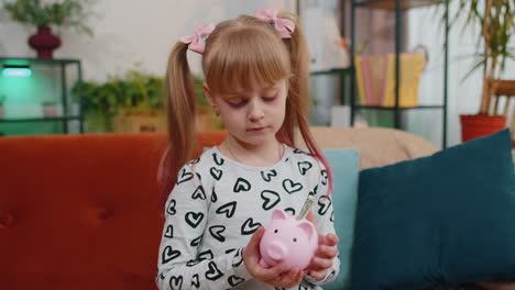 Frustrated-poor-little-kid-girl-hold-almost-empty-piggybank-with-only-one-dollar-cash,-bankruptcy