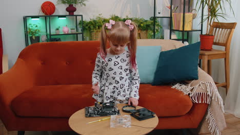 Little-girl-kid-fixing-repairing-computer-mainboard-technology-part,-using-magnifying-glass-at-home