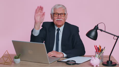 Senior-business-man-waves-hand-palm-in-hi-gesture-greeting-welcomes-someone-webinar-at-pink-office