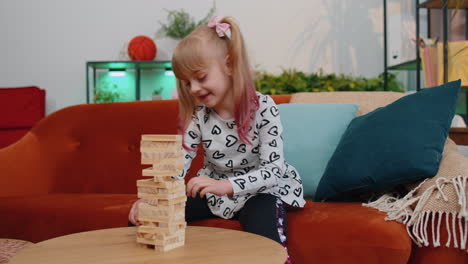 Funny-happy-one-teenage-kid-girl-play-wooden-tower-blocks-bricks-game-at-home-in-modern-living-room