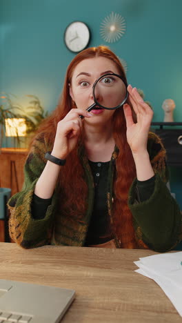 Amazed-woman-holds-magnifying-glass-near-face-looking-at-camera-with-big-zoomed-eye-analyzing-wow