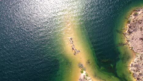 Drone-footage-showing-the-coast-meeting-a-stunning-blue-lake-at-Whiskeytown-Reservoir,-California