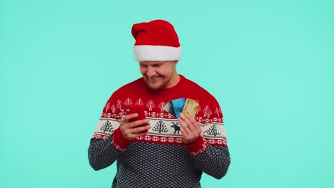 Mann-Im-Weihnachtlichen-Roten-Pullover-Benutzt-Mobiltelefon,-Kreditkarten-Aus-Plastik,-Gewinnt,-Kalebriert,-Wow