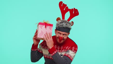 Funny-man-wears-New-Year-sweater-deer-antlers-received-present,-interested-in-what-inside-gift-box