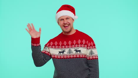 Man-in-red-Christmas-sweater-waves-hand-palm-in-hello-gesture-welcomes-someone-to-celebrate-New-Year