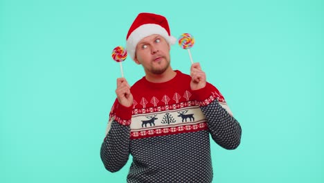 Funny-man-in-red-New-Year-sweater,-hat-holding-candy-striped-lollipops,-dancing,-making-silly-faces