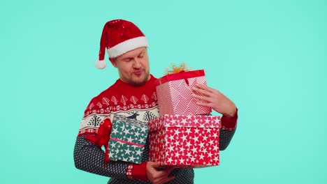 Lovely-man-in-Christmas-red-sweater-hat-presenting-Christmas-gift-boxes-stretches-out-hand-to-camera