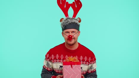 Funny-man-wears-red-New-Year-sweater-and-deer-antlers-presenting-Christmas-gift-box,-shopping-sale