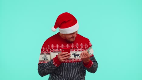 Mann-Im-Weihnachtsroten-Pullover-Benutzt-Mobiltelefon-Und-Plastik-Kreditkarte,-Gewinnt,-Kalebriert,-Wow