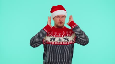 Man-in-Christmas-sweater-covering-ears-and-gesturing-no,-avoiding-advice-ignoring-unpleasant-noise