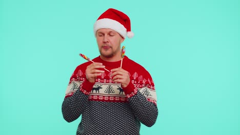 Joyful-man-in-red-New-Year-sweater,-hat-holding-candy-striped-lollipops,-dancing,-making-silly-faces