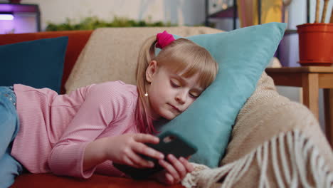 Child-toddler-hold-smartphone-watching-funny-cartoons,-chatting-with-friends-on-couch-alone-at-home