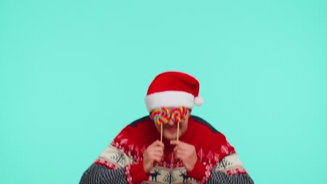 Funny-man-in-red-New-Year-sweater-holding-candy-striped-lollipops-hiding-behind-them,-fooling-around