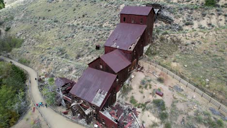 Rusted-Gold-mine-and-Mill-building,-panoramic-aerial-view-with-people-walking
