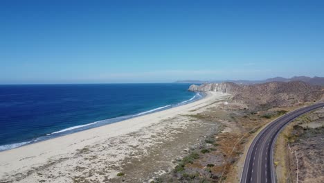 Drone-footage-of-Cabo-San-Lucas-and-Todos-Santos-road-in-Baja-California-Sur-Mexico,-with-clear-blue-ocean-waters-and-mountains-in-the-distance