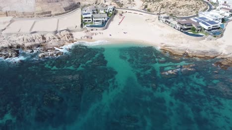 Drone-footage-of-Playa-Boca-del-Tule-Cabo-San-Lucas-Baja-California-Sur-Mexico,-with-clear-ocean-water-and-a-few-buildings-on-the-beach