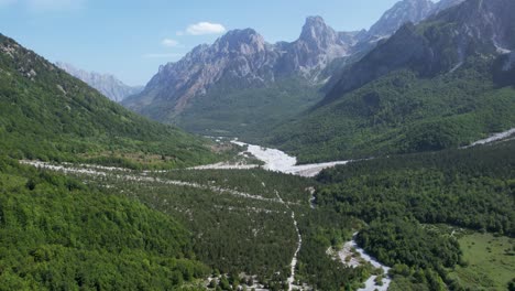 Valbona-Valley-of-Alpine-Beauty,-A-Riverbed-Meanders-Through-Stones,-Surrounded-by-Lush-Green-Forests-and-Rocky-Peaks-in-Albania