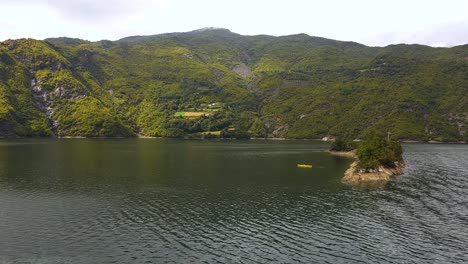 Las-Aguas-Del-Lago-Atraen-A-Los-Kayakistas-Cerca-De-La-Isla,-Ubicada-En-Un-Valle-Rodeado-De-Majestuosas-Montañas-Rocosas-En-Koman,-Albania