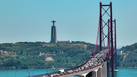 Traffic-At-The-25-de-Abril-Bridge-Over-The-Tagus-River-With-The-Christ-the-King-Sanctuary-In-Lisbon,-Portugal