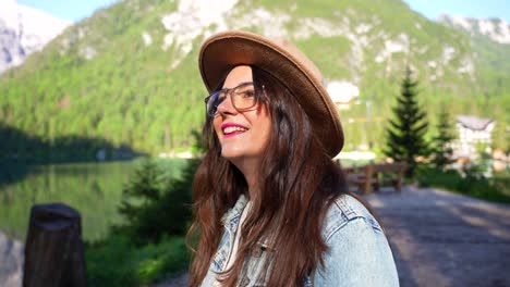 Woman-with-brown-hat-turns-and-smiles-at-camera-in-Lago-di-Braies-forested-area,-Italy