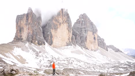 Solo-man-jumps-up-in-excitement-at-base-of-Dolomiti-with-snowy-Tre-Cime-di-Lavaredo-behind