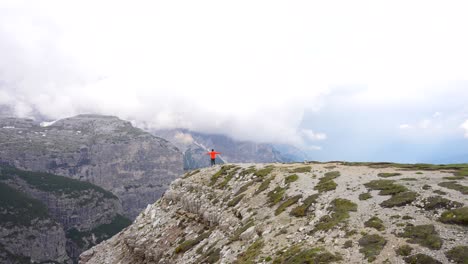 Man-in-jacket-runs-to-cliff-edge-arms-outstretched-admiring-beauty-of-Auronzo-Valley