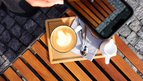 Girl-capture-multiple-photos-of-latte-foam-art-on-wooden-outdoor-table