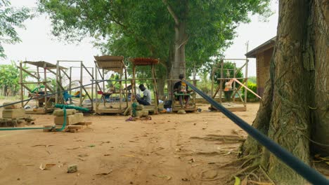 Afrikanische-Männer-Weben-Kente-Textilien-Auf-Rustikalen-Webstühlen-Zwischen-Bäumen-Im-Dorf-Ghana