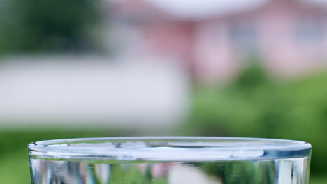 Droplets-of-water-hitting-the-surface-of-crystal-clear-water-in-a-transparent-glass-cup-on-a-blurry-background