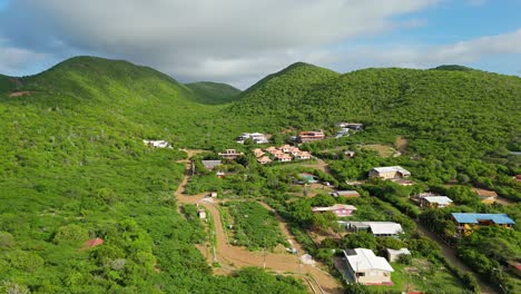Homes-sprawl-up-into-valley-of-Westpunt-in-Curacao-on-tropical-sunny-day,-aerial