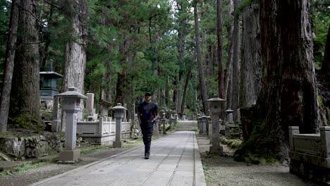 Solo-Male-Backpacker-Casually-Walking-Along-Path-Through-Zen-Forest-Cemetery-In-Japan