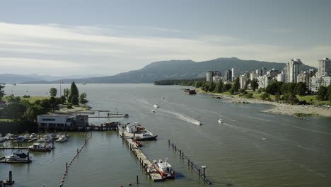 Panoramic-view-from-Burrard-Bridge-over-Sunset-Beach-in-Vancouver,-with-ships-passing-and-Stanley-Park-in-the-distance,-in-slow-motion