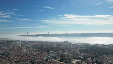 Aerial-view:-Lisbon's-coastal-dwellings,-25-April-Bridge,-and-foggy-allure—a-captivating-daytime-canvas-in-Portugal