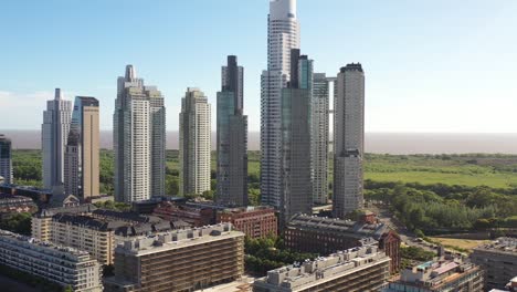 Towering-skyscrapers-rise-above-the-treeline-in-Buenos-Aires,-with-the-vast-Rio-de-la-Plata-in-the-backdrop