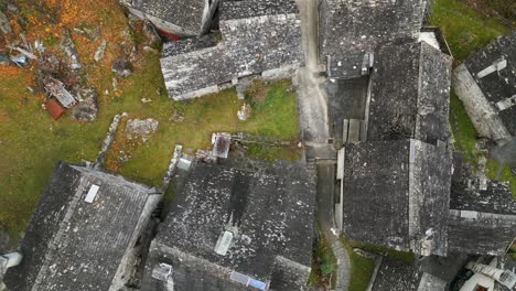 Aerial-drone-zoom-out-shot-over-old-empty-village-house-roofs-in-Cavergno,-District-of-Vallemaggia,-Canton-of-Ticino-in-Switzerland-at-daytime